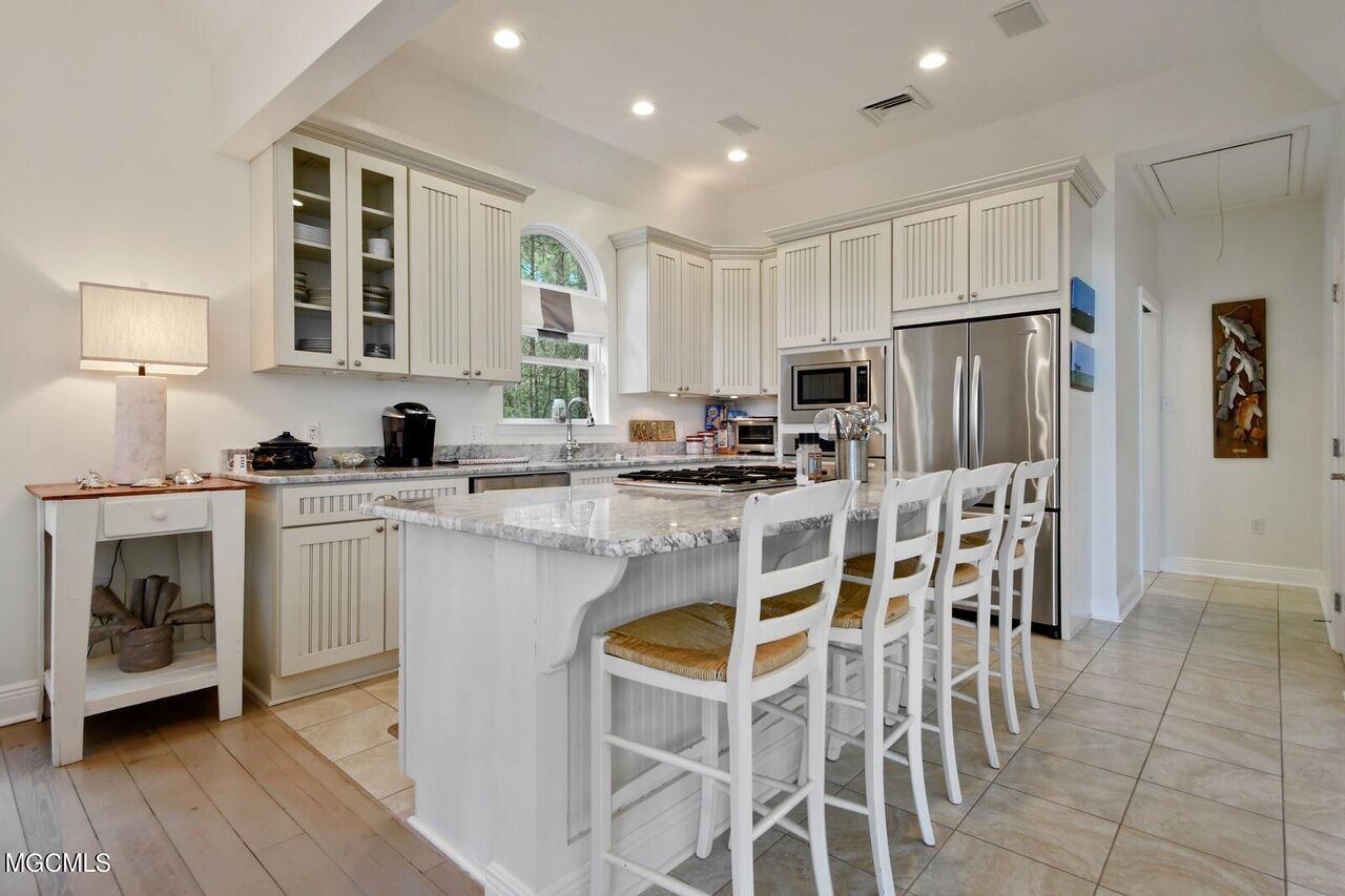 A spacious kitchen with white cabinetry, a large island with bar stools, and modern appliances.