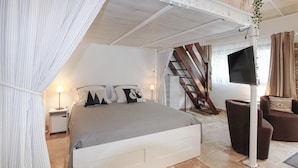 Een slaapkamer met een bed, nachtlampen, een televisie, een trap en een groot raam.