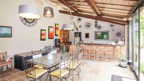 Een ruime eethoek met een glazen tafel en stoelen, een houten plafond en diverse wanddecoraties.