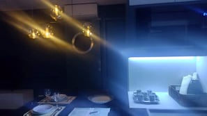 Une pièce faiblement éclairée, avec une table dressée pour le repas, un luminaire au plafond et un appareil de climatisation fixé au mur.