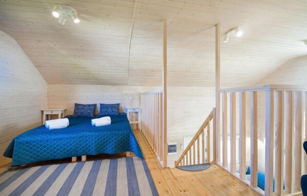 Une chambre mansardée chaleureuse, avec un plafond en pente, un lit avec une literie bleue, un tapis à rayures et un escalier en bois.
