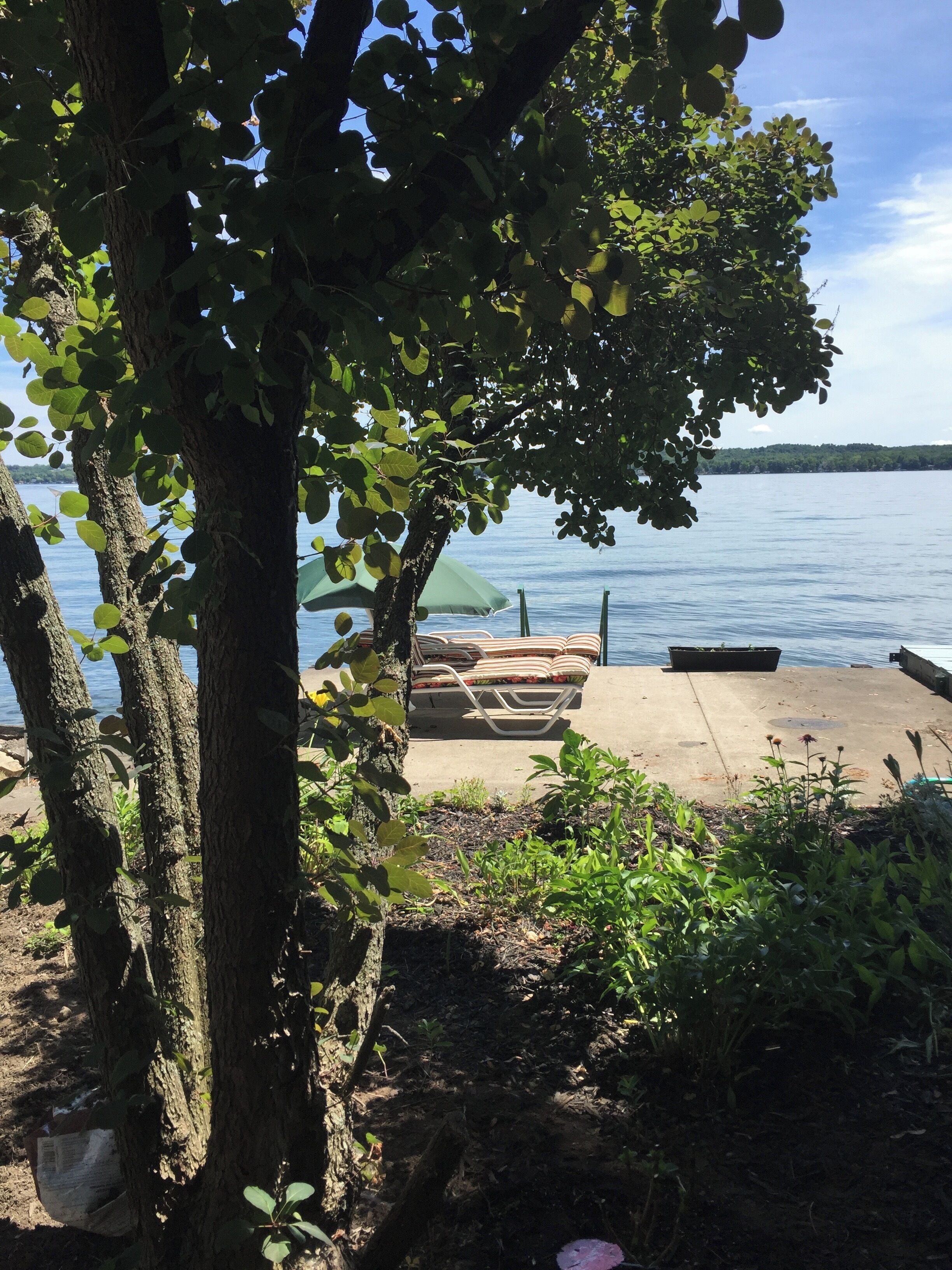 Une vue sur le lac, avec un quai en béton, un fauteuil de relaxation et une petite table.