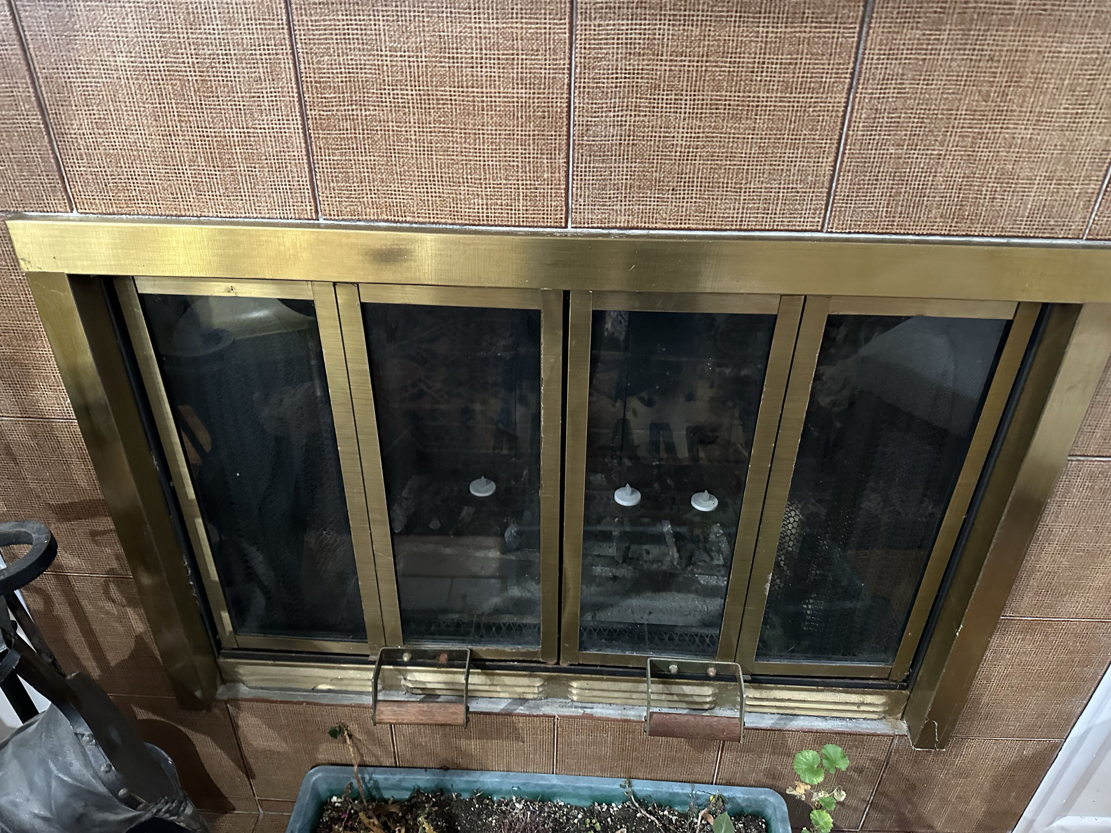 A sliding glass door with a brass frame, a small planter with plants, and a textured wall.