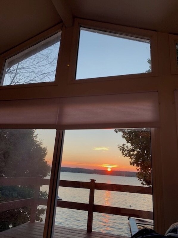 A room with large windows overlooking a sunset over a body of water.
