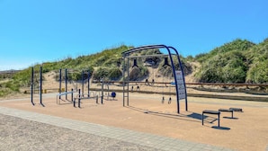 An outdoor exercise area with various fitness equipment, including a climbing wall and pull-up bars, surrounded by a sandy area and vegetation. - Awesome home in Falkenberg (Falkenberg)