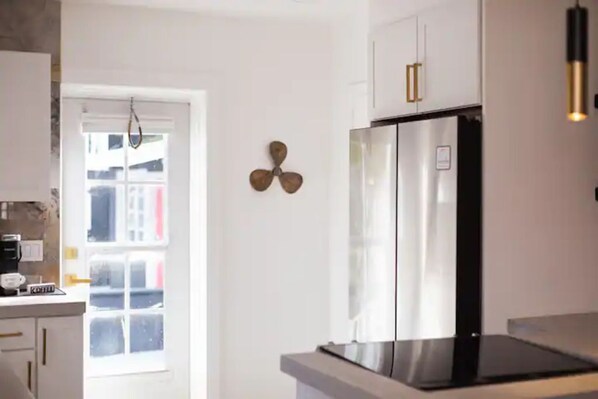 A modern kitchen with white cabinets, a stainless steel refrigerator, and a coffee machine.