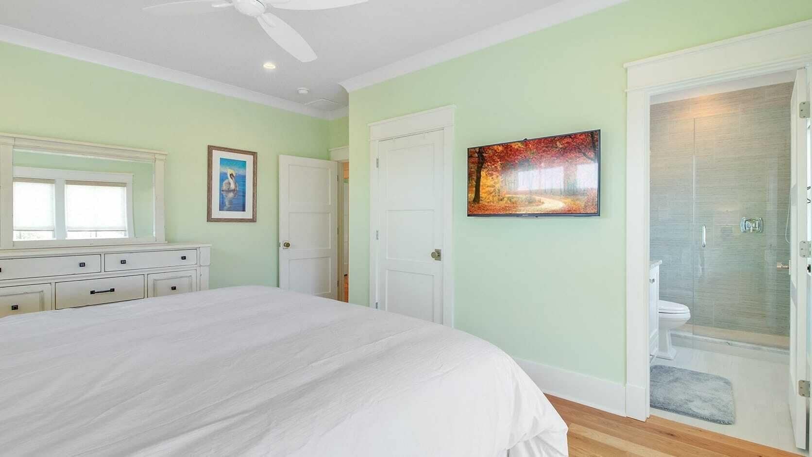 Ein Schlafzimmer mit einem großen Bett, einem Schminktisch, einem Gemälde und einem Badezimmer mit einer Duschkabine.