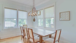 A dining area with a wooden table and chairs, large windows, and a hanging light fixture. - 616 Carolina Boulevard by Avantstay Ocean Views From Decks (Isle of Palms)