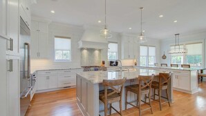 A spacious kitchen with white cabinetry, a large island with bar stools, and pendant lighting. - 616 Carolina Boulevard by Avantstay Ocean Views From Decks (Isle of Palms)