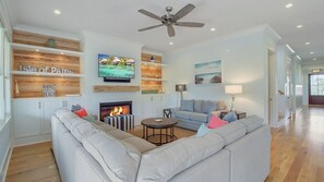 A living room with a fireplace, sofas, a television, and a ceiling fan.