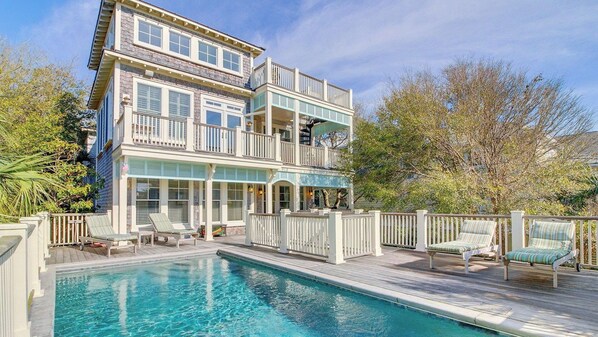 A two-story house with a pool, outdoor furniture, and a fenced deck.