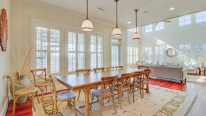 A dining area with a wooden table and chairs, large windows, and a view of the outdoors.