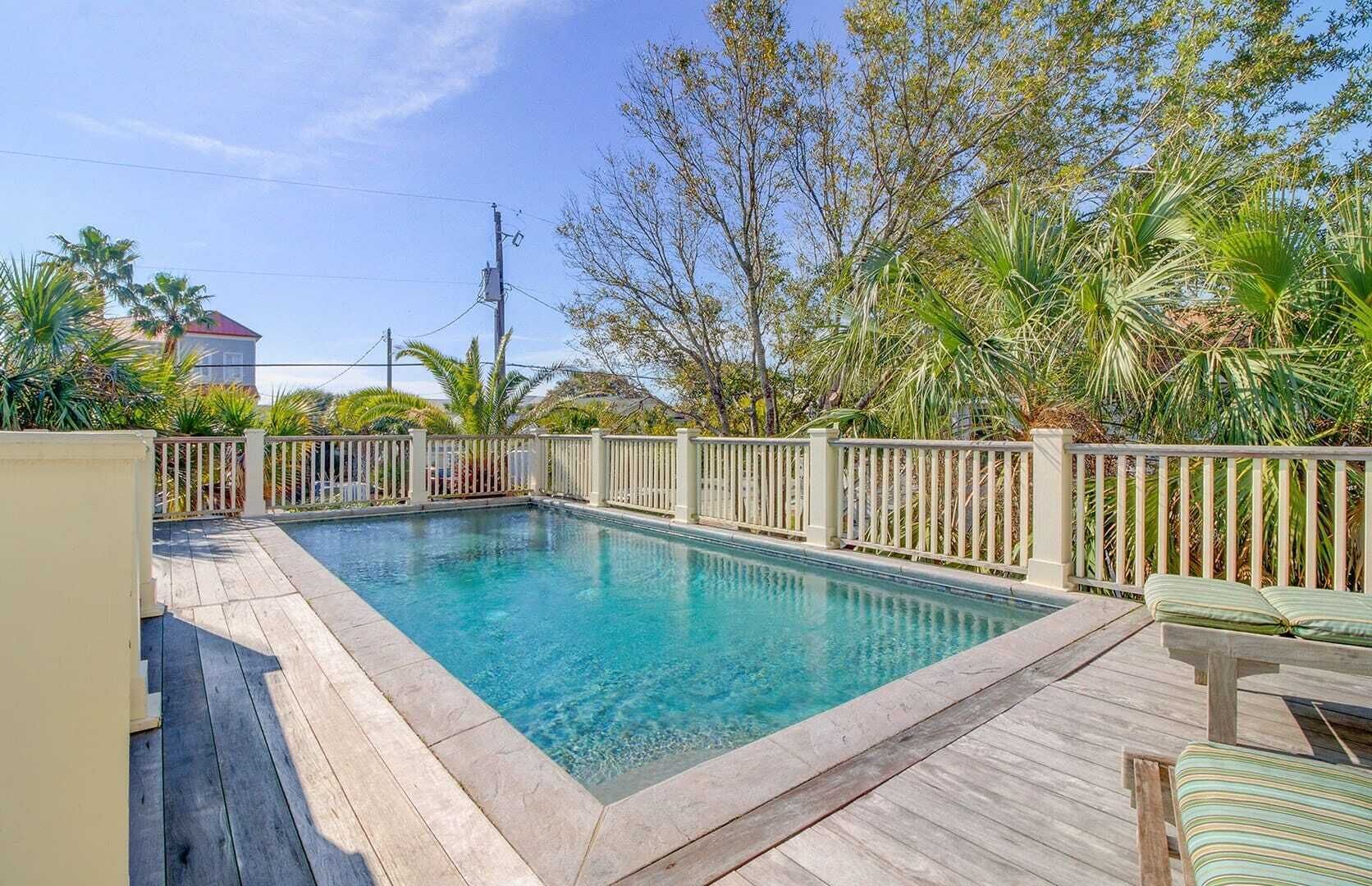 A rectangular swimming pool with a wooden deck and white picket fence.
