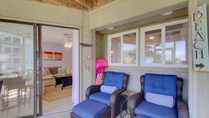 A covered outdoor seating area with wicker chairs and a bench, a glass door leading to an interior living space, and a 'BEACH' sign on the wall.