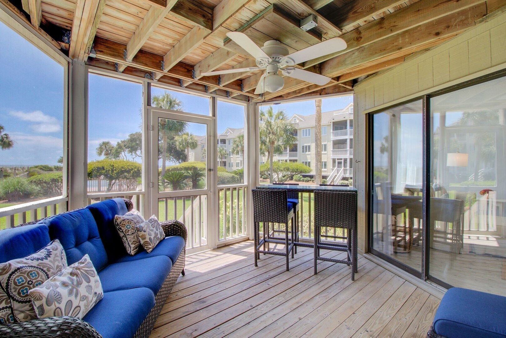 A covered outdoor area with a blue sofa, wicker chairs, a table, and a ceiling fan.
