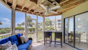 A covered outdoor area with a blue sofa, wicker chairs, a table, and a ceiling fan.