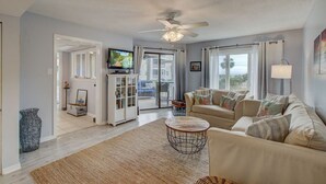 A spacious living room with a beige sofa, a television, and a ceiling fan.