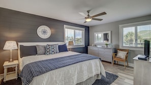 A bedroom with a bed, bedside table, lamp, dresser, chair, and a ceiling fan.