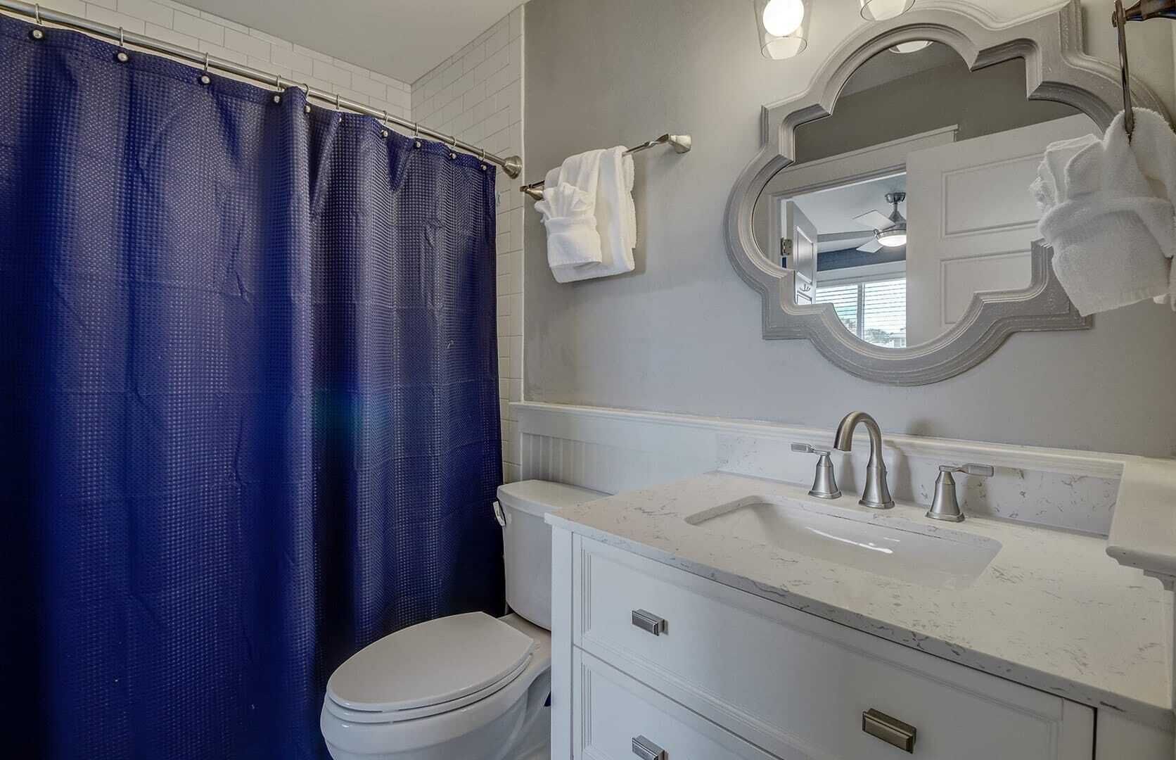 A bathroom with a white toilet, a sink with a mirror above it, and a blue shower curtain.
