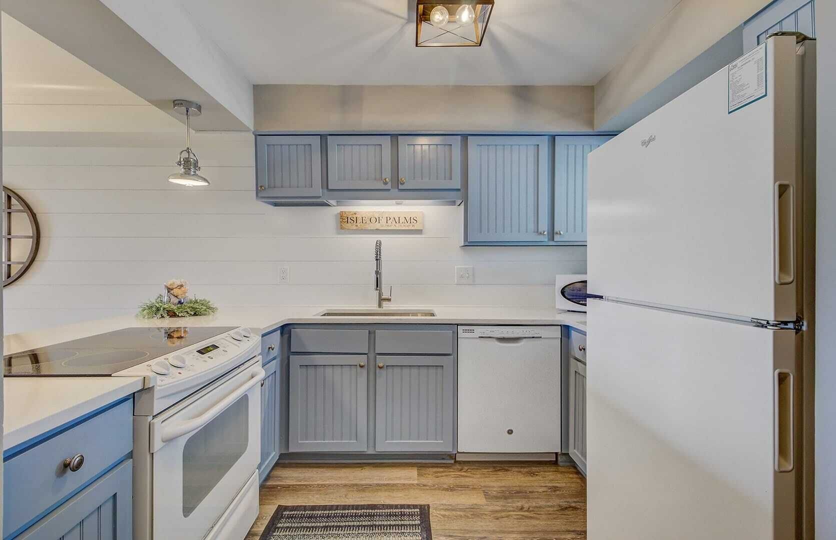 A compact kitchen with blue cabinets, a white refrigerator, and a built-in dishwasher.