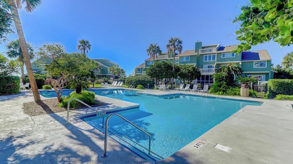 A swimming pool with lounge chairs, palm trees, and a multi-story building in the background.