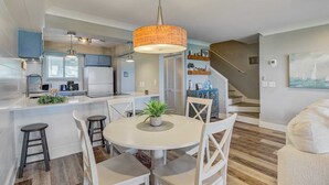 A modern kitchen with white cabinets, a central island, and a hanging orange pendant light. - 11B Mariners Walk by Avantstay Direct Beach Access! Views Communal Pool (Isle of Palms)