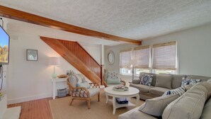 Ein gemütliches Wohnzimmer mit einer Holztreppe, einem Sofa, einem Couchtisch und einem Sessel.