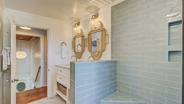 Ein Badezimmer mit einer blauen Duschkabine, einem weißen Waschtisch inklusive Spiegel und einem Holzboden.