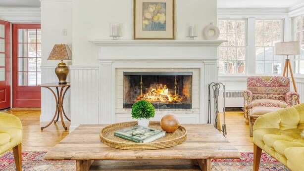Una sala de estar con chimenea, una mesa de centro con libros y un cuenco decorativo, un sillón estampado y una lámpara.