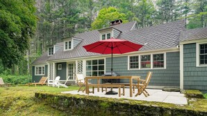 Una casa con un patio que cuenta con una mesa y sillas de madera, un paraguas rojo y una parrilla.