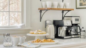 Una encimera de cocina con una cafetera, un hervidor y un plato de cruasanes.
