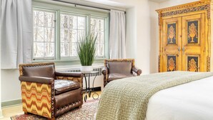 Un dormitorio con cama, dos sillones, un armario de madera, una ventana con cortinas y una planta en maceta.