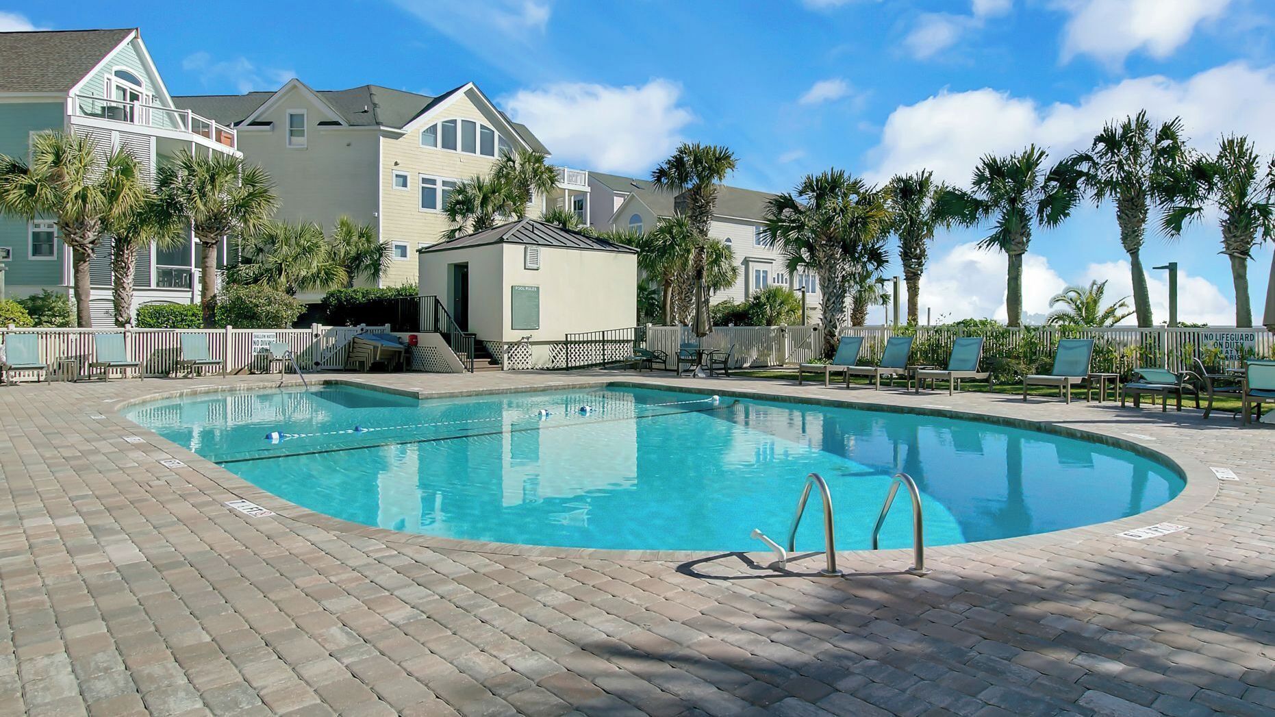 A swimming pool with lounge chairs, a lifeguard tower, and a building with a balcony.