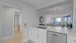 A modern kitchen with white cabinetry, a built-in dishwasher, and a large island with a sink. - 207 Summerhouse by Avantstay Beachfront Community w/ Ocean Views! (Isle of Palms)