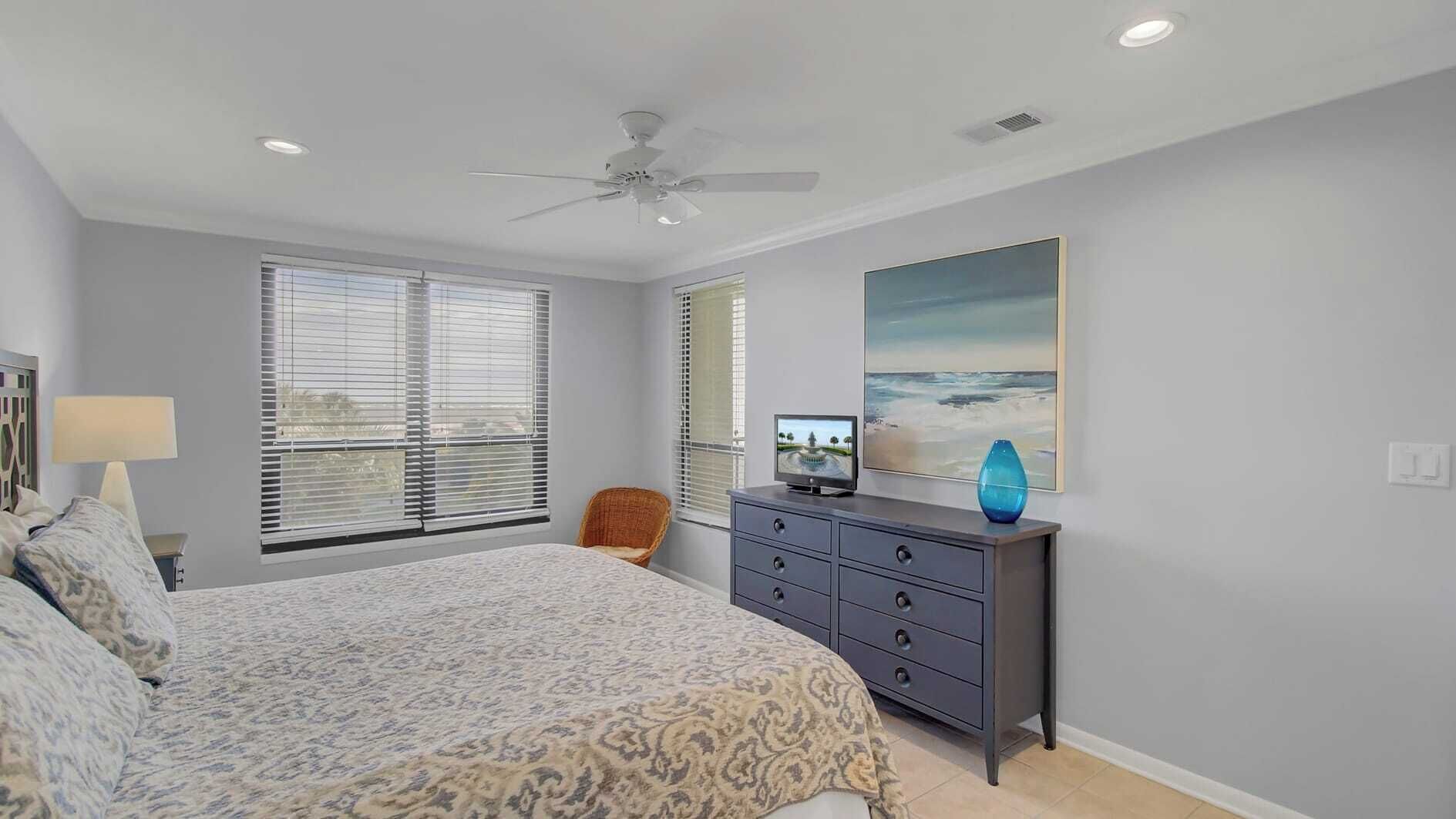 A bedroom with a bed, a dresser, a chair, and a ceiling fan.