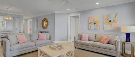 A living room with two sofas, a coffee table, a ceiling fan, abstract wall art, and a mirror.