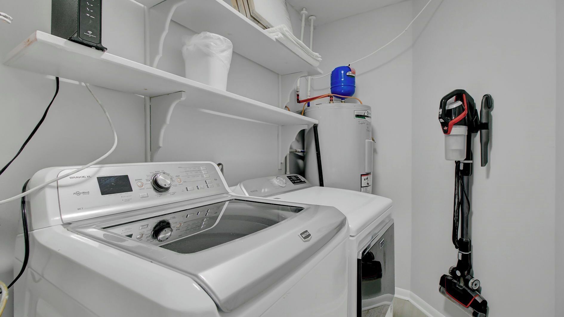 A laundry area with a front-loading washing machine, a wall-mounted vacuum cleaner, and a water heater.