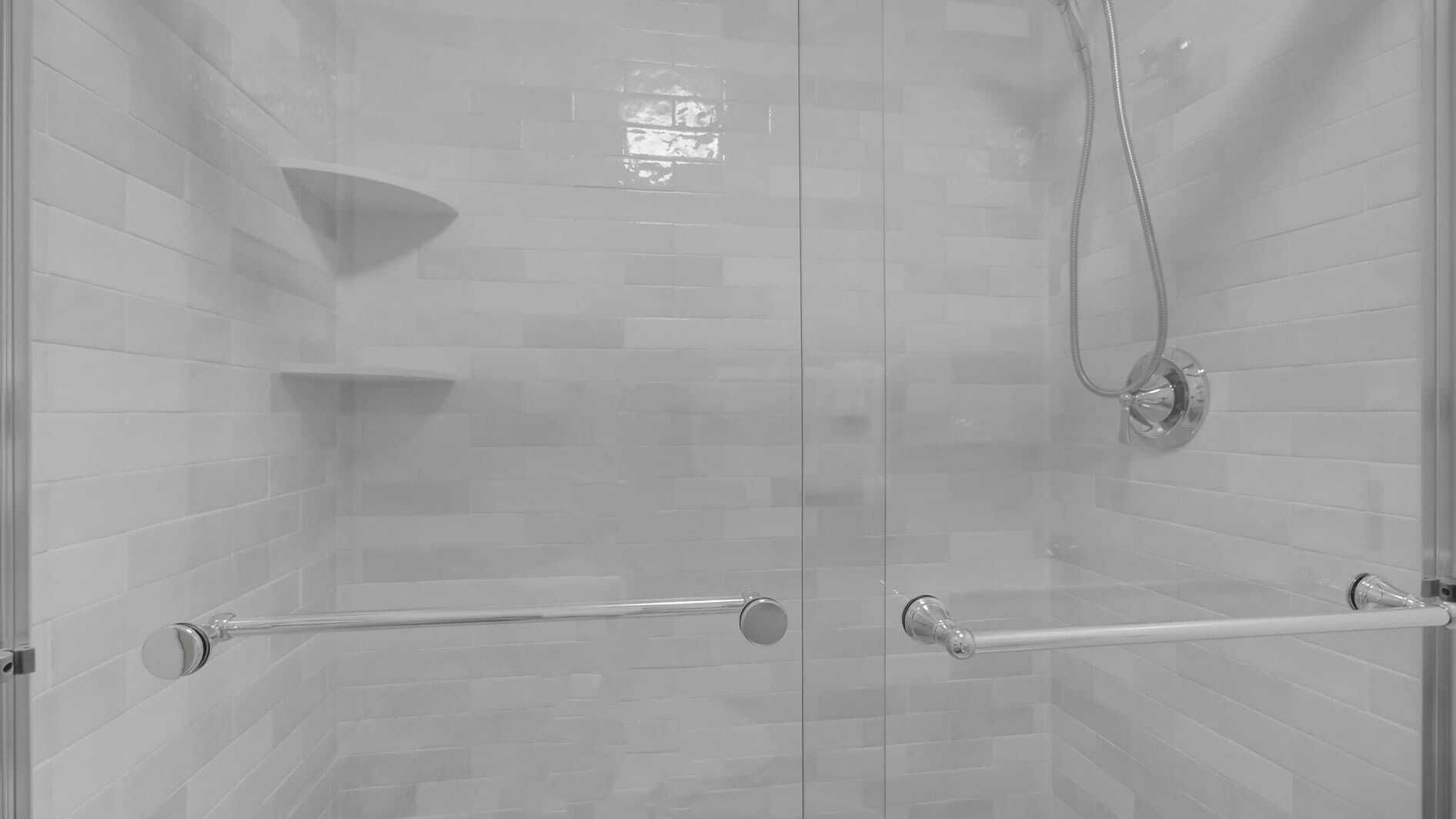 Una ducha con puerta de cristal, un cabezal de ducha manual y un perchero para toallas.