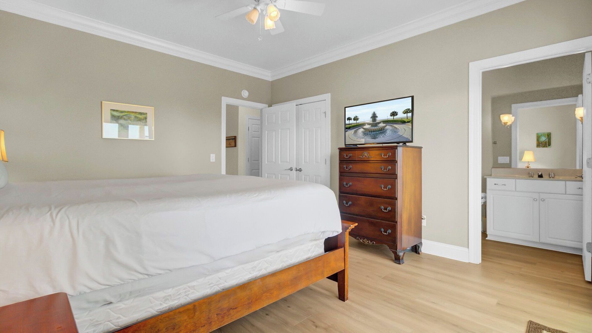 Une chambre à coucher avec un grand lit, une commode, un téléviseur et une salle de bain équipée d’un lavabo et d’un miroir.