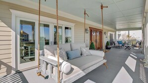 Une véranda avec une balançoire, un canapé blanc avec des coussins et un coin repas avec des chaises et des tables.