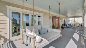 A covered porch with a swing, a white sofa with cushions, and a dining area with chairs and tables.