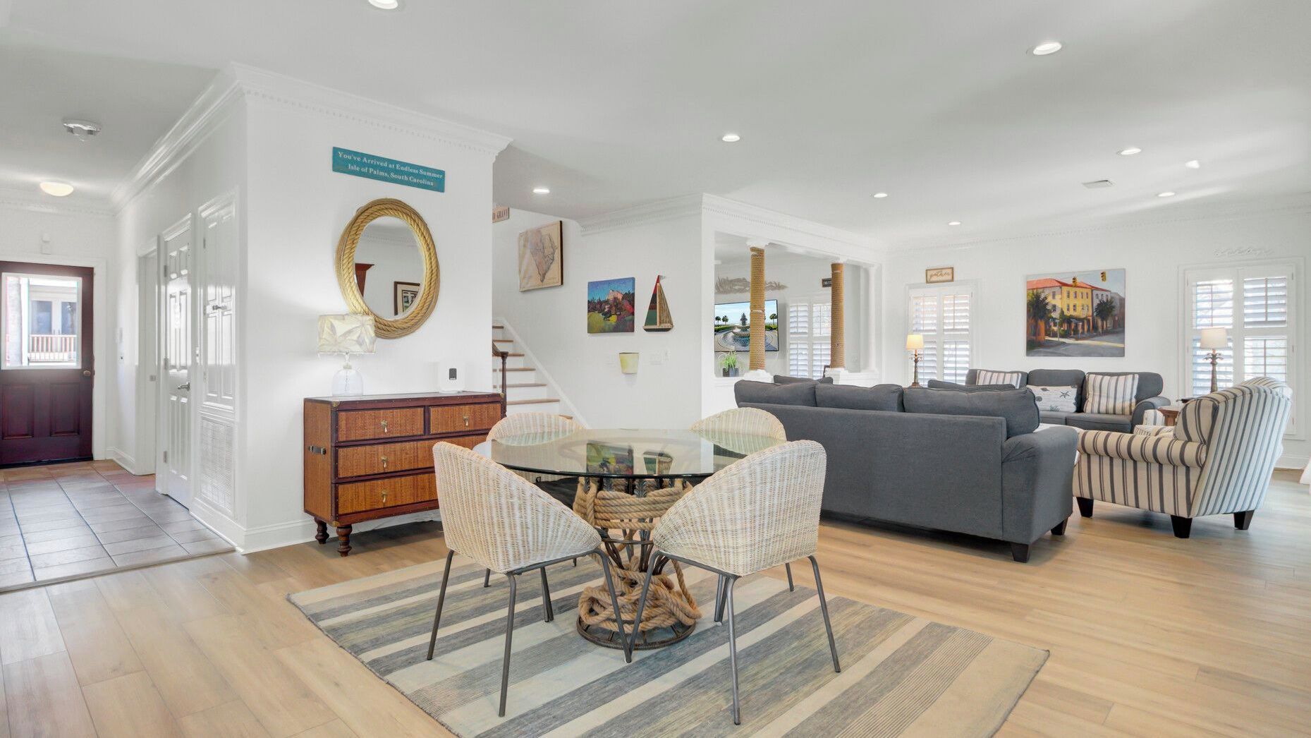 A spacious living room with a gray sofa, wicker chairs, a glass-top dining table, and a staircase leading to another level.