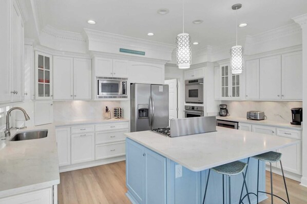 Una cocina moderna con armarios blancos, electrodomésticos de acero inoxidable, una isla azul y dos taburetes de bar.