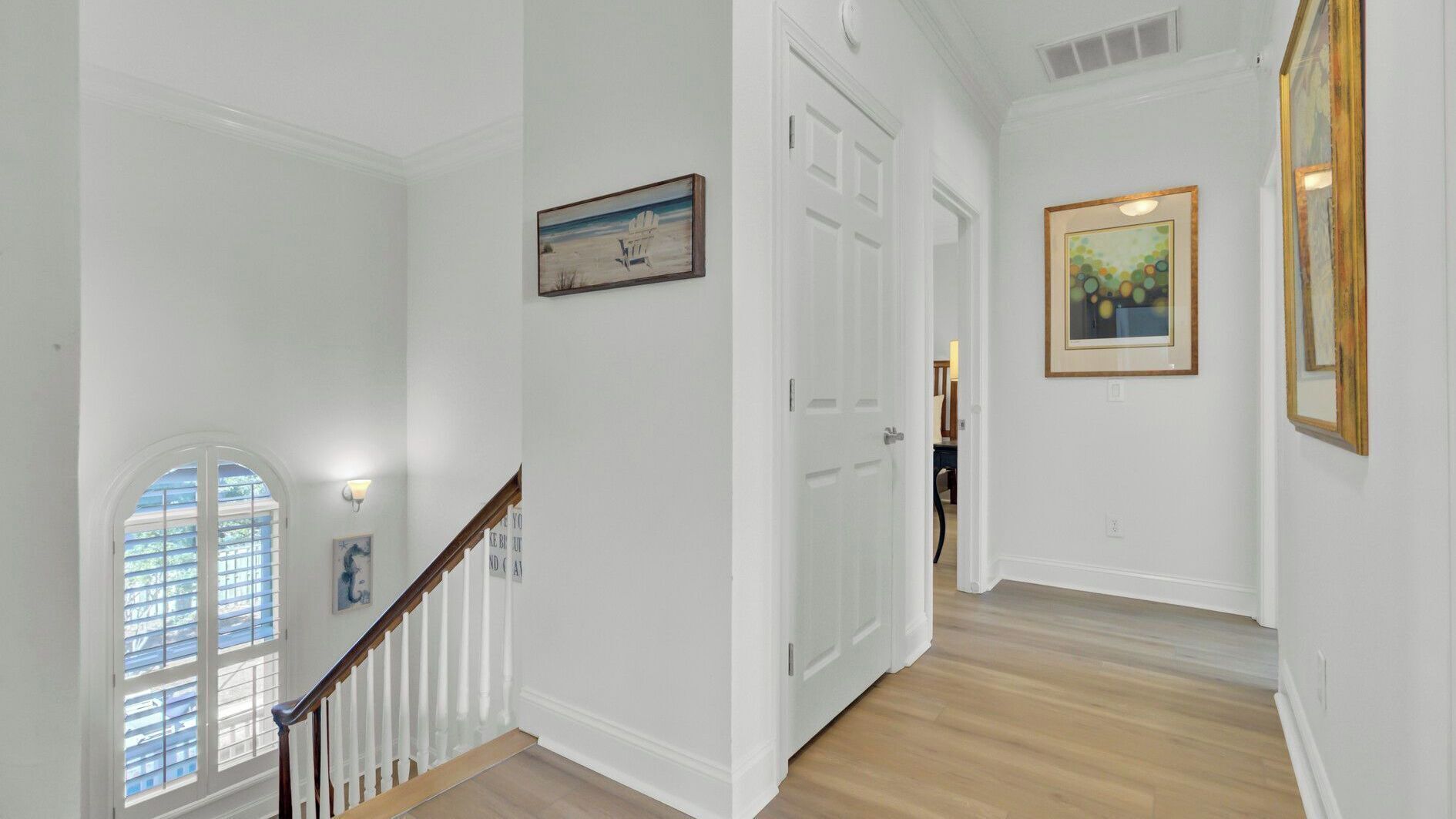 A hallway with white walls, a wooden staircase, and a door leading to another room.