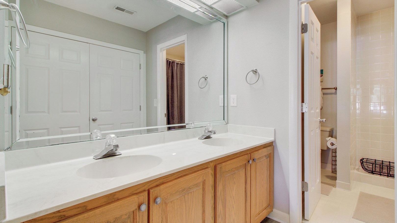 A bathroom with a double sink, wooden cabinets, a large mirror, and a shower area.