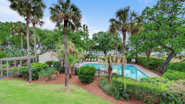 A pool surrounded by palm trees and lush greenery, with a gazebo and lounge chairs in the background. - 405 Yacht Harbor by Avantstay Marina Views + Pool Access + Outdoor Lounge Near Golf & Beach (Isle of Palms)