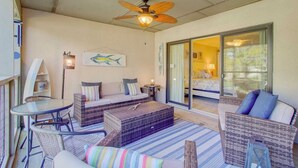 A sunlit room with wicker furniture, a ceiling fan, and a large sliding glass door leading to a bedroom. - 405 Yacht Harbor by Avantstay Marina Views + Pool Access + Outdoor Lounge Near Golf & Beach (Isle of Palms)