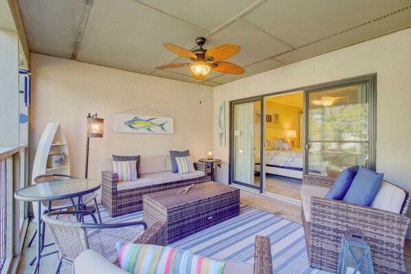 A sunlit room with wicker furniture, a ceiling fan, and a large sliding glass door leading to a bedroom. - 405 Yacht Harbor by Avantstay Marina Views + Pool Access + Outdoor Lounge Near Golf & Beach (Isle of Palms)