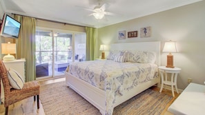A bedroom with a bed, a television, a chair, a table, and a lamp.