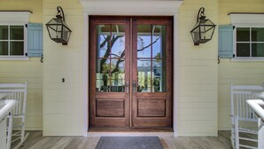 A wooden double door with glass panels, flanked by white railings and two wall-mounted lanterns.